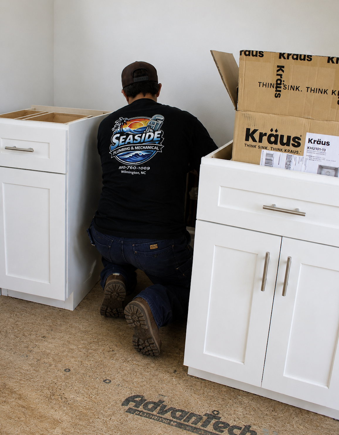 Plumber installing a sink. Two white cabinets are on the sides of him.
